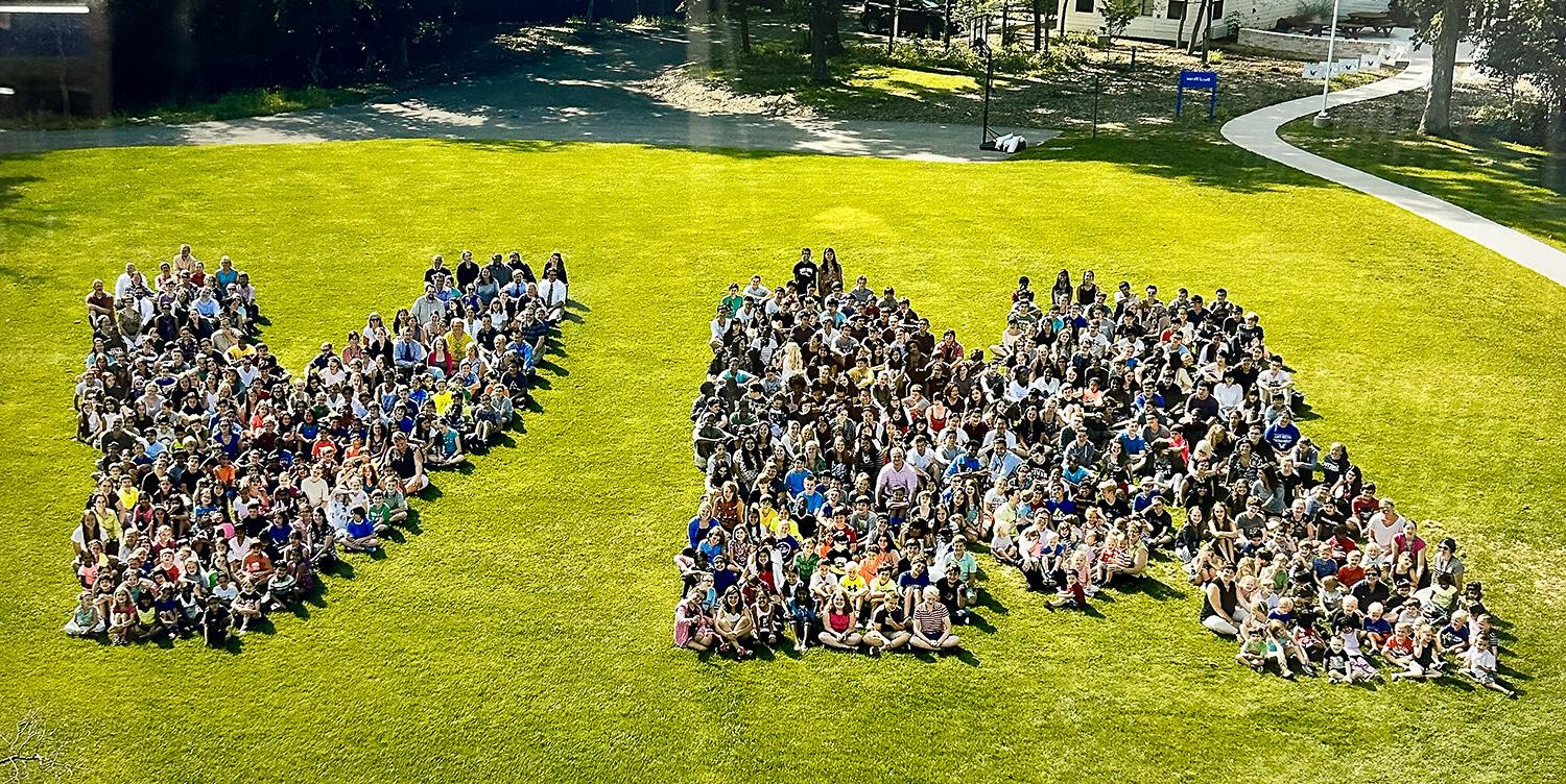 学生们坐在草地上形成MV的形状